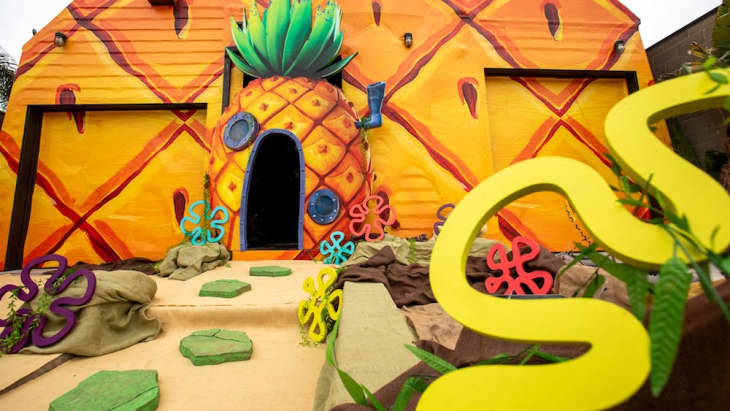 Building facade painted as a pineapple with colorful flower decorations and green stepping stones.