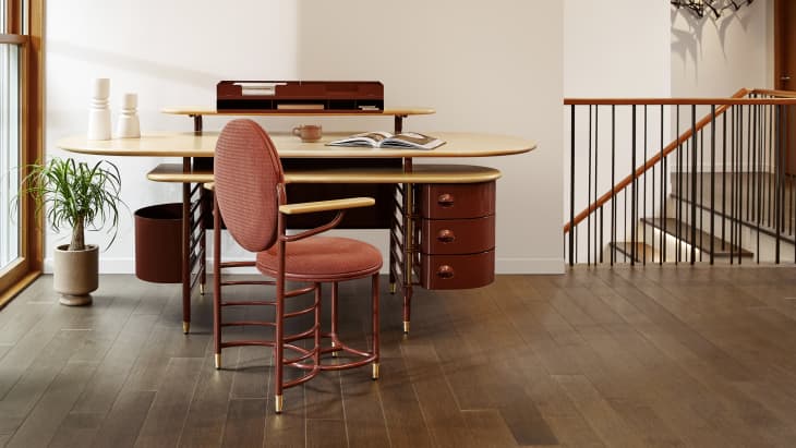 Mid-century modern desk with red drawers, matching chair, potted plant, and open book in a bright room.