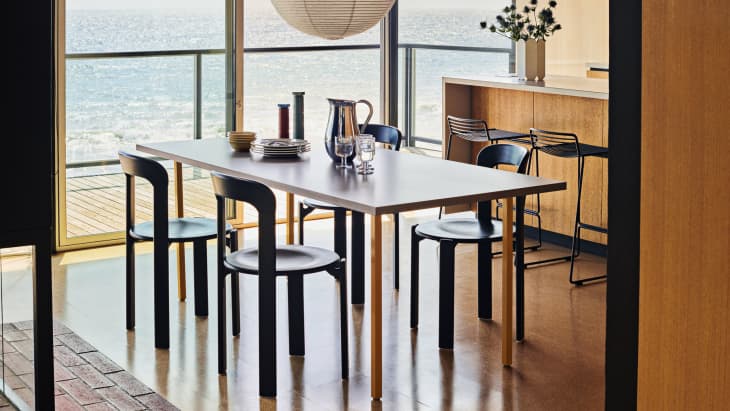 Dining area with a table set for four, overlooking an ocean view, featuring modern black chairs and a wooden bar with stools.