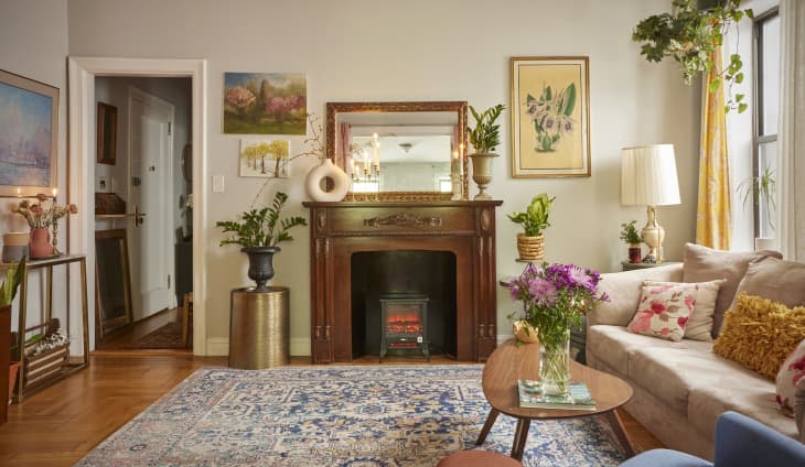 Fireplace mantel in Brooklyn apartment filled with plants. Mantel is topped with mirror, vases, plants and taper candles and surrounded by artwork.