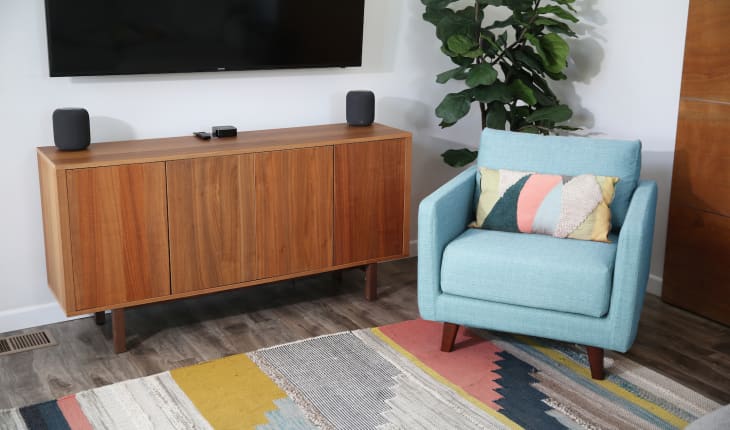 Mid-century modern living room with a wooden sideboard, blue armchair, colorful rug, and a large potted plant.