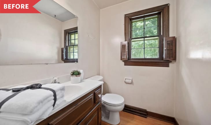 Small bathroom with wooden vanity, white countertop, towels, potted plant, and window with shutters.