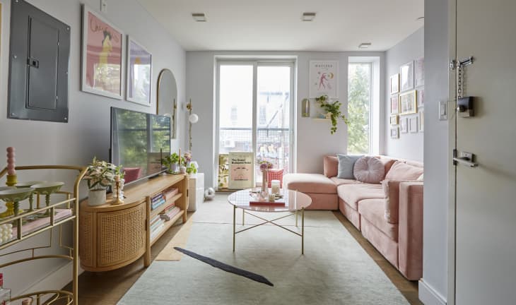 Living room with pink sectional sofa, round glass coffee table, wall art, and a TV on a wooden console.