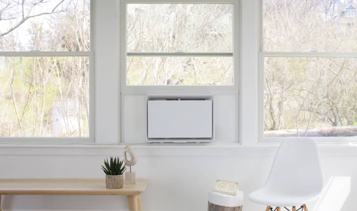 Minimalist room with large windows, a white air conditioner, wooden bench with a plant, and a white chair.