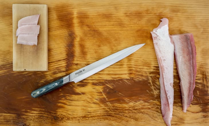 Sliced fish fillets on a wooden board with a chef's knife beside them.