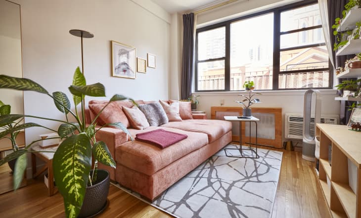 living room with wood floors, peach/pink velvet sofa, plants, large windows, wood shelves, white walls and white beamed ceiling