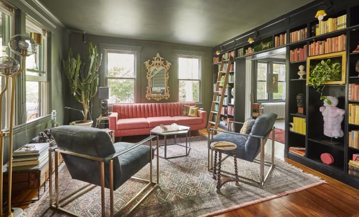 Eclectic living room with pink sofa, cactus, dark bookshelves, ladder, and vintage decor.