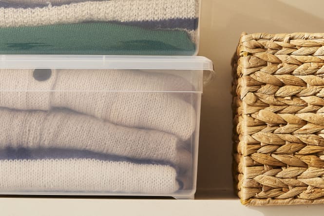 Sweaters folded and stored in plastic storage bin on shelf next to straw storage basket
