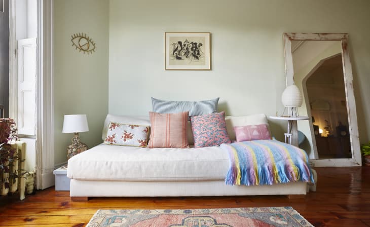 Cream sofa with colorful cushions, striped throw, and a large mirror in a cozy living room with wooden floors.