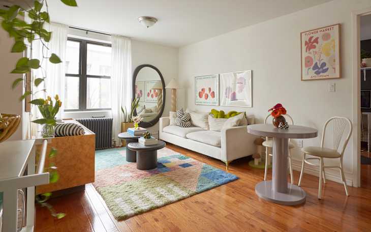 A south-facing window in an apartment living room with white walls, a white couch, and a colorful rug and artwork