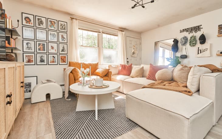 living room with large off-white sectional sofa with peach and warm hued pillows and throw, grid-style gallery wall