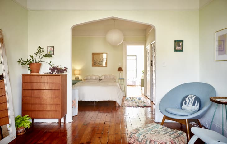 Mid-century modern bedroom with wooden dresser, potted plants, blue chair, and a bed with striped pillows.