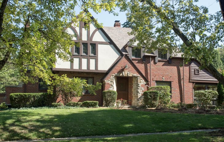 Tudor-style brick house with gabled roof, surrounded by trees and shrubs.