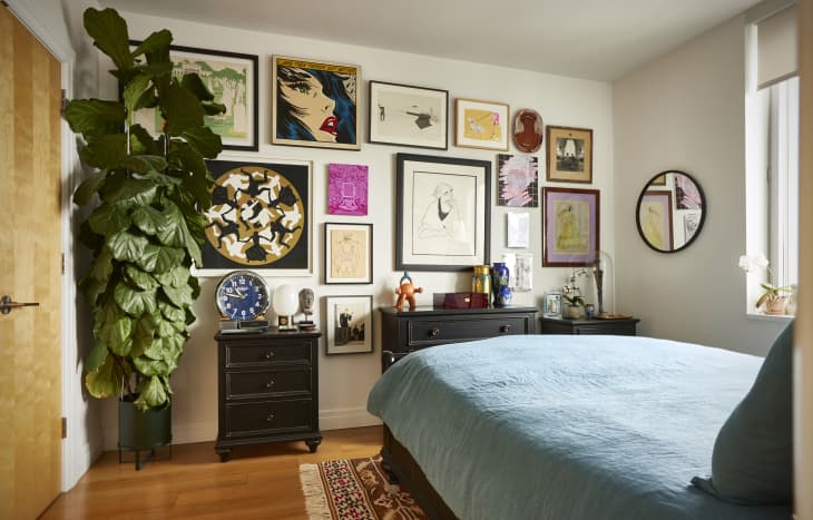 A bedroom wall with a gallery wall and a bed with blue sheets.