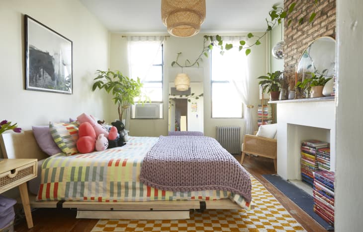 A small bedroom with books piled in the clean white fireplace
