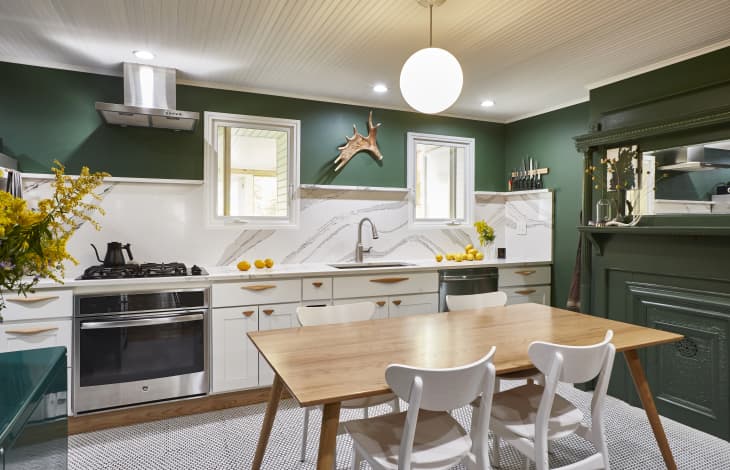 Kitchen with green walls, wooden table, white chairs, marble backsplash, and yellow flowers on the counter.