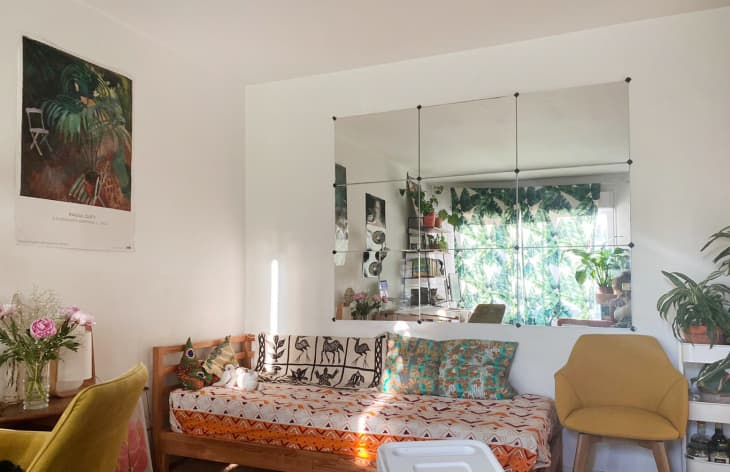 Living room with a patterned daybed, yellow chair, large mirror, and plants.