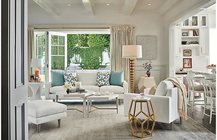 Bright living room with white sofas, blue cushions, geometric side table, and open French doors to a garden view.