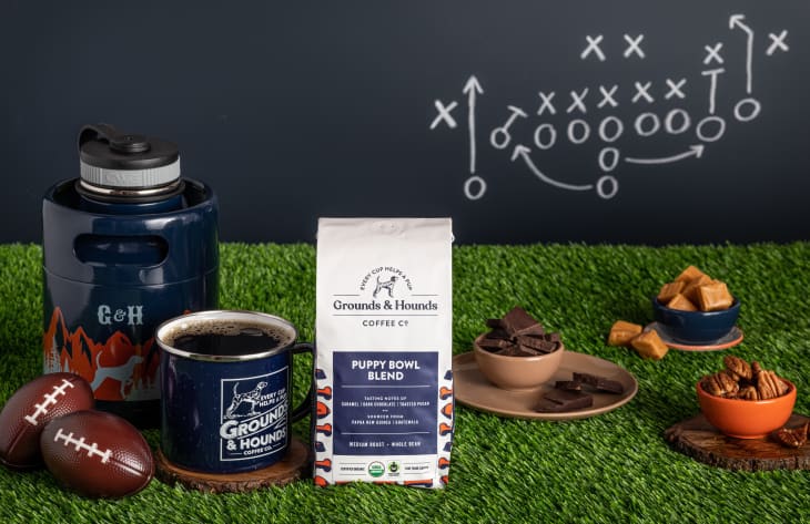 Grounds & Hounds Puppy Bowl Blend coffee with footballs, mug, and snacks on artificial grass, chalkboard play diagram in background.