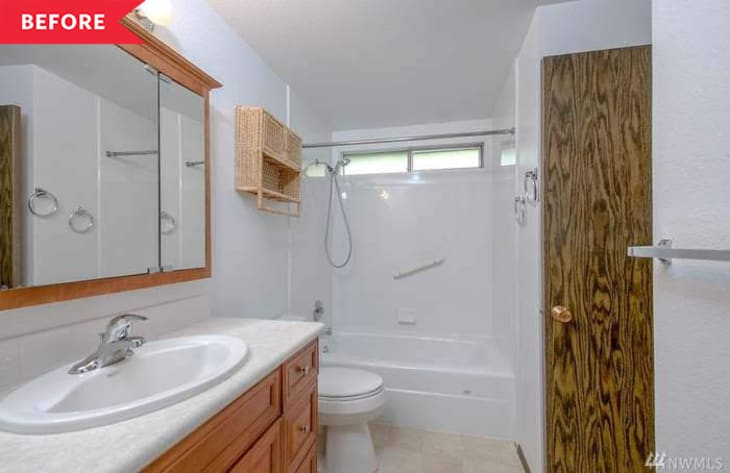 Small bathroom with wood vanity, mirror, wicker shelf, bathtub, and showerhead.