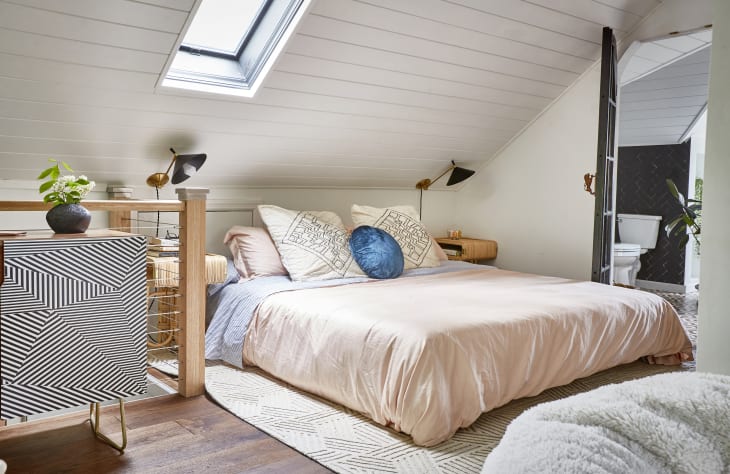 Attic bedroom with skylight, pink bedding, blue accent pillow, geometric cabinet, and modern decor.
