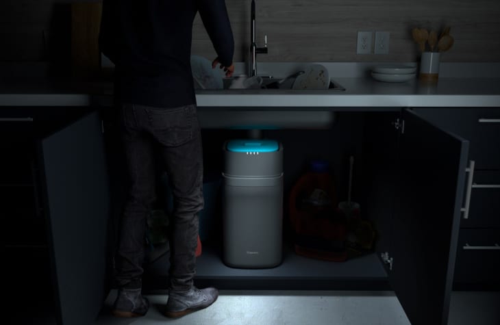 Person standing at a kitchen sink with a garbage disposal unit glowing blue under the cabinet.