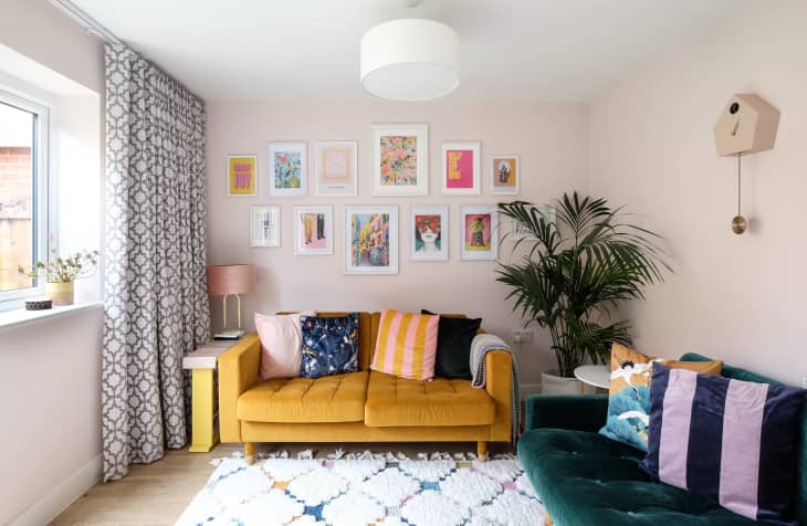 gallery wall above yellow couch, geometric pattern curtains, striped throw pillows, teal velvet couch, cuckoo clock on wall, white rug with pastel diamond pattern, large fern in corner