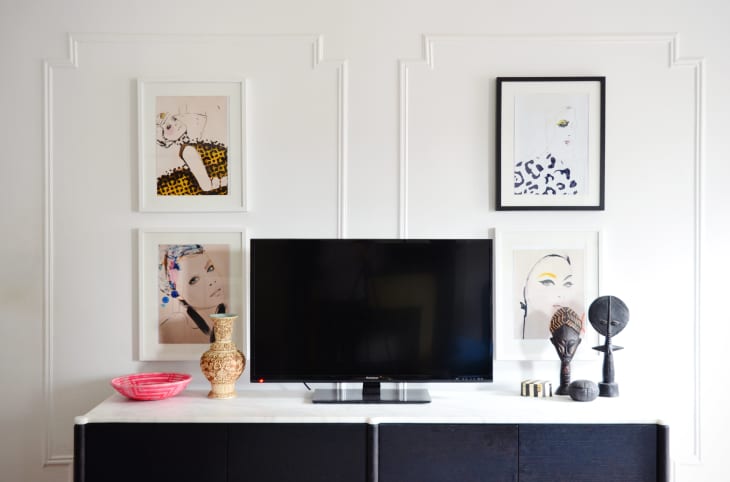 TV on a black console with framed art, decorative vases, and sculptures on a white wall.