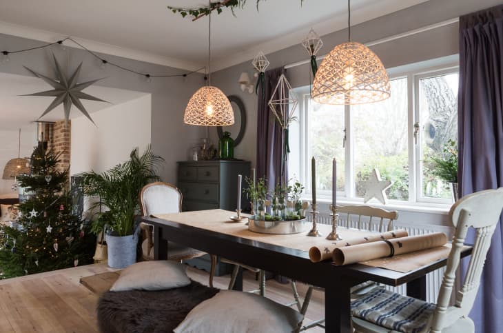 Dining room with a wooden table, pendant lights, Christmas tree, and festive decor, including candles and greenery.