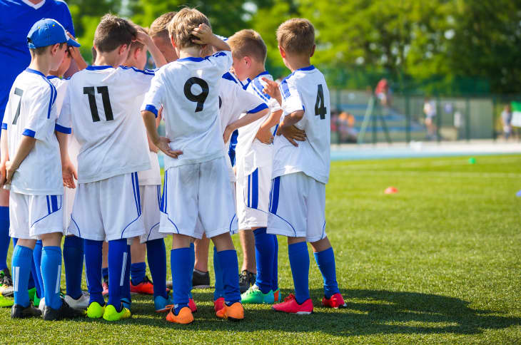 A group of young soccer players in white jerseys with blue accents huddled together on a grassy field.
