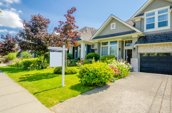 Front view of a house with a well-maintained garden, colorful flowers, and a "For Sale" sign.