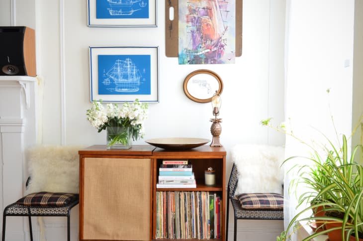 Mid-century modern console with books, records, floral vase, and abstract art, flanked by two chairs with plaid cushions.