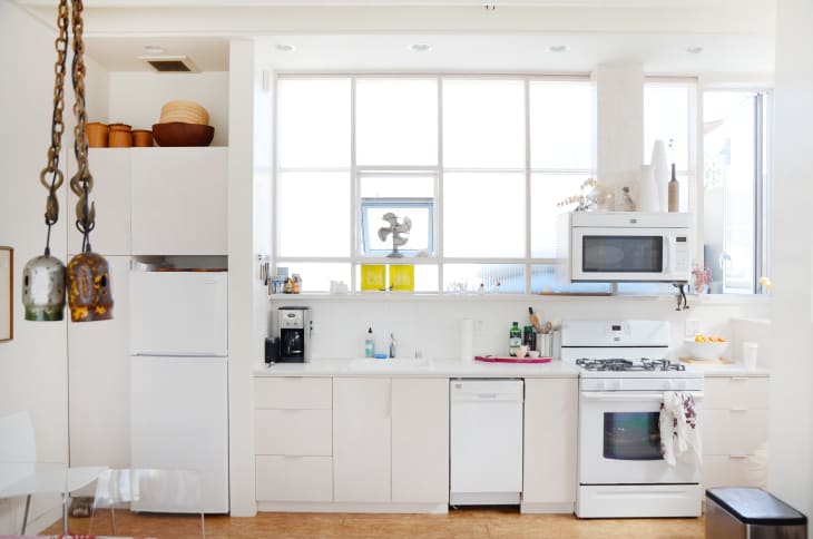 Bright kitchen with white cabinets, a gas stove, microwave, and hanging decorative bells.