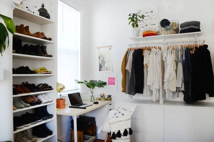 Home office with a desk, laptop, potted plant, shoe rack, and clothes hanging on a wall-mounted rack.