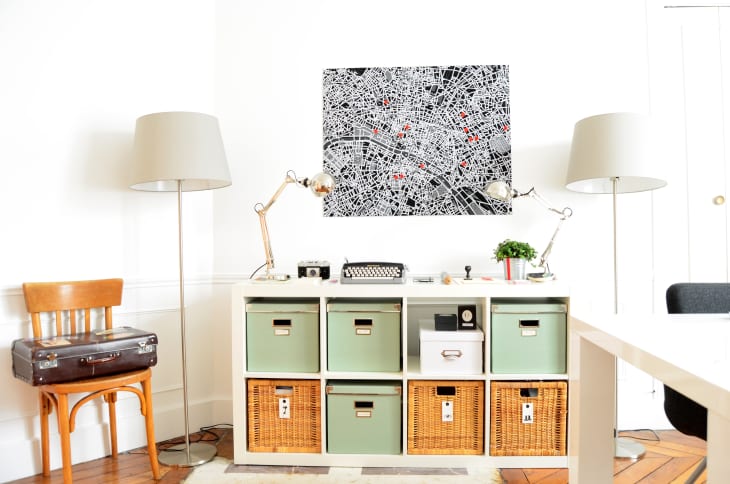 Home office with a typewriter on a white desk, green storage boxes, wicker baskets, and a city map artwork on the wall.