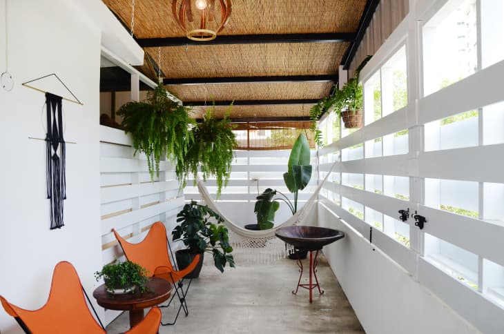 Enclosed patio with hanging plants, hammock, orange chairs, and a small table.