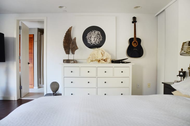 An acoustic guitar hanging on the wall next to a white IKEA dresser in a bedroom