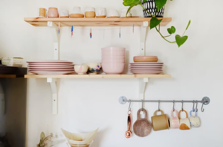 Open kitchen shelves with pink dishes, mugs, wooden cutting boards, and a hanging plant.