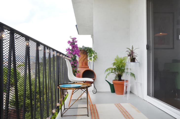 Balcony with a white chair, small table, potted plants, and a clay chiminea, overlooking greenery.
