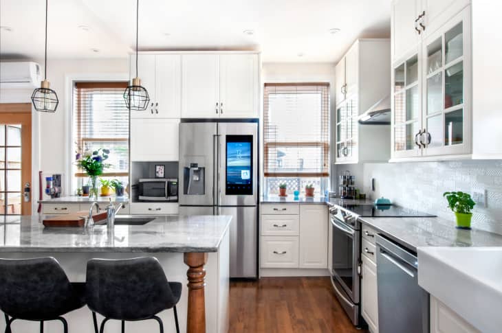 A modern white kitchen with stone countertops and stainless steel appliances