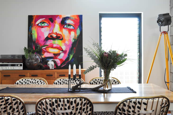 Dining room with colorful portrait, wooden sideboard, polka dot chairs, and a vase of flowers on the table.