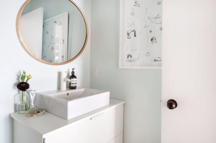 Bathroom with round mirror, white sink, soap dispenser, and flower vase on a white vanity.