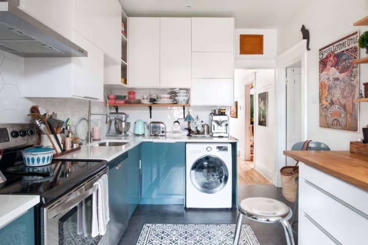 Modern kitchen with white cabinets, blue lower cabinets, washing machine, and vintage posters on the walls.