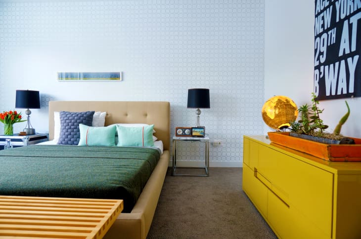 Modern bedroom with a beige bed, green bedding, yellow dresser, black lamps, and a globe decor piece.