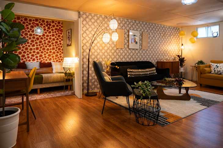 living area in basement with gold and black sofas, fireplace, wood floor, black and white area rugs, plants