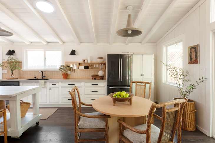 Bright kitchen featuring a round wooden table with a bowl of green apples, rustic chairs, and modern appliances.