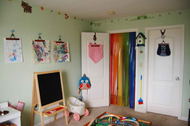 Children's playroom with art on clipboards, chalkboard easel, rainbow bead curtain, and colorful wall decor.