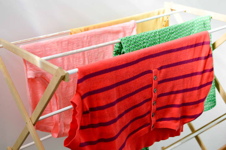 Colorful shirts drying on a wooden clothes rack indoors.