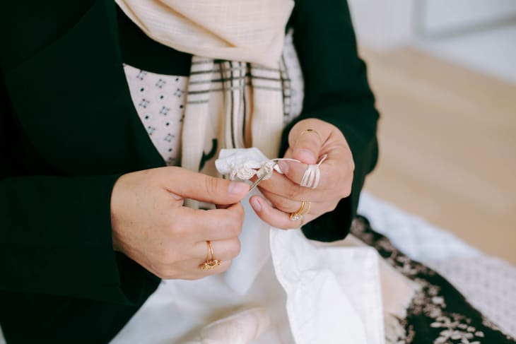 Hands holding a small white tassel, wearing rings and a patterned scarf.