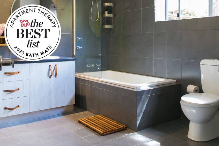 Gray tile bathroom with wood slat bath mat. Seal in upper left that reads "Apartment Therapy the Best List 2023 Bath Mats"